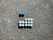 Colourful marbles arranged on a five by five grid. There are two blue marbles in the first row, in the first and second columns. There is no second row. In the third row the first two columns are empty, the remaining columns are occupied by white marbles. The fourth and fifth rows are filled with white marbles.