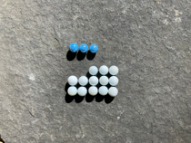 Colourful marbles arranged on a five by five grid. There are three blue marbles in the first row. There is no second row. In the third row the first two columns are empty, the remaining columns are occupied by white marbles. The fourth and fifth rows are filled with white marbles.