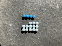 Colourful marbles arranged on a five by five grid. There are four blue marbles in the first row. There is no second row. In the third row the first two columns are empty, the remaining columns are occupied by white marbles. The fourth and fifth rows are filled with white marbles.