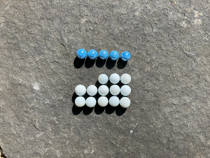 Colourful marbles arranged on a five by five grid. The first row is filled with blue marbles. There is no second row. In the third row the first two columns are empty, the remaining columns are occupied by white marbles. The fourth and fifth rows are filled with white marbles.