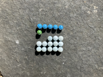 Colourful marbles arranged on a five by five grid. The first row is filled with blue marbles. There is a single green marble in the second row. In the third row the first two columns are empty, the remaining columns are occupied by white marbles. The fourth and fifth rows are filled with white marbles.