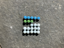 Colourful marbles arranged on a five by five grid. The first row is filled with blue marbles. There are three green marbles in the second row. In the third row the first two columns are empty, the remaining columns are occupied by white marbles. The fourth and fifth rows are filled with white marbles.