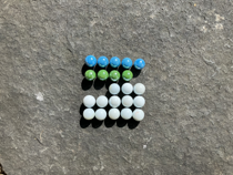 Colourful marbles arranged on a five by five grid. The first row is filled with blue marbles. There are four green marbles in the second row. In the third row the first two columns are empty, the remaining columns are occupied by white marbles. The fourth and fifth rows are filled with white marbles.