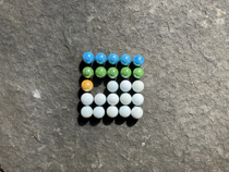 Colourful marbles arranged on a five by five grid. The first row is filled with blue marbles. The second row is filled with green marbles. In the third row the first column has a yellow marble in it, the second is empty, the remaining columns are occupied by white marbles. The fourth and fifth rows are filled with white marbles.