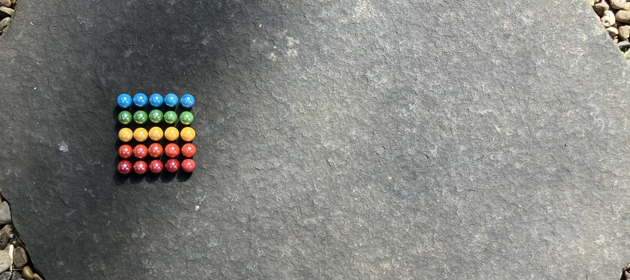 Colourful marbles arranged on a five by five grid. The first row is blue, the second row is green, the third row is yellow, the fourth row is orange and the fifth row is red.