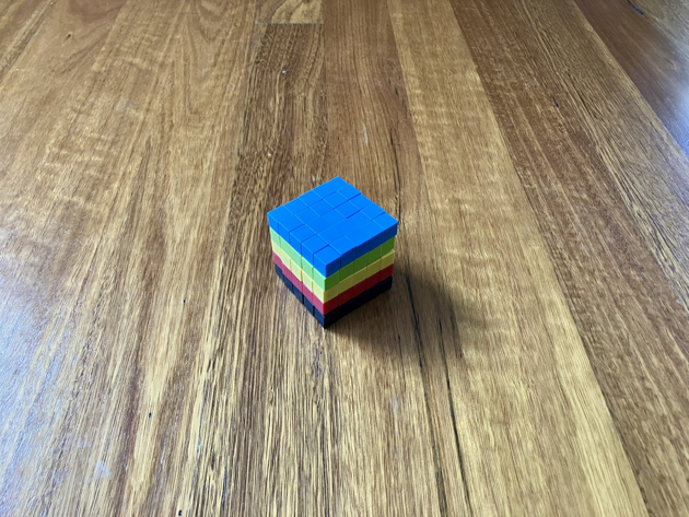 Colourful magnetic blocks, arranged in a cube, five wide, five high and five deep. Each layer has a different colour of magnetic block. Top to bottom it goes: blue, green, yellow, red and black.