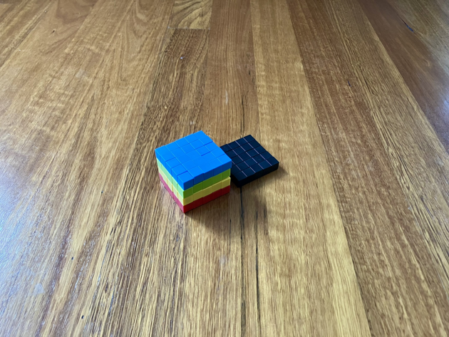 Colourful magnetic blocks, arranged in a rectangular prism, five wide, five high and four deep. Each layer has a different colour of magnetic block. Top to bottom it goes: blue, green, yellow, and red. A black five by five square of blocks sits just behind.