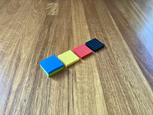 Colourful magnetic blocks, arranged in a rectangular prism, five wide, five high and two deep. Each layer has a different colour of magnetic block. The top is blue, and the bottom is green. Three five by five squares of blocks sit just behind, one yellow, one red and one black.