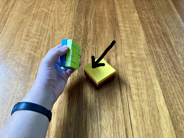 Colourful magnetic blocks, arranged in a cube, five wide, five high and five deep. The top two layers have been removed to reveal the yellow layer, an arrow is pointing to the block one in from the side and the top.